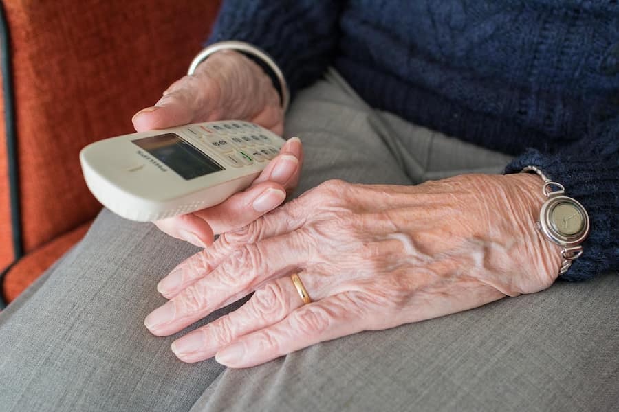An older person's hands are holding a cordless phone 